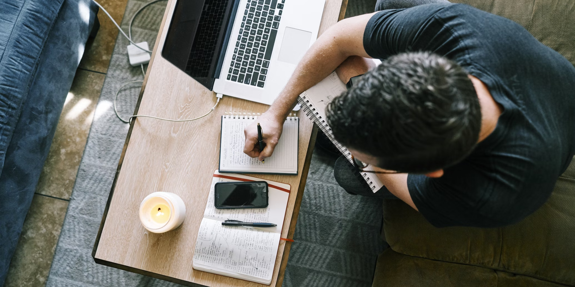 view from above of a person taking notes on paper next to their laptop